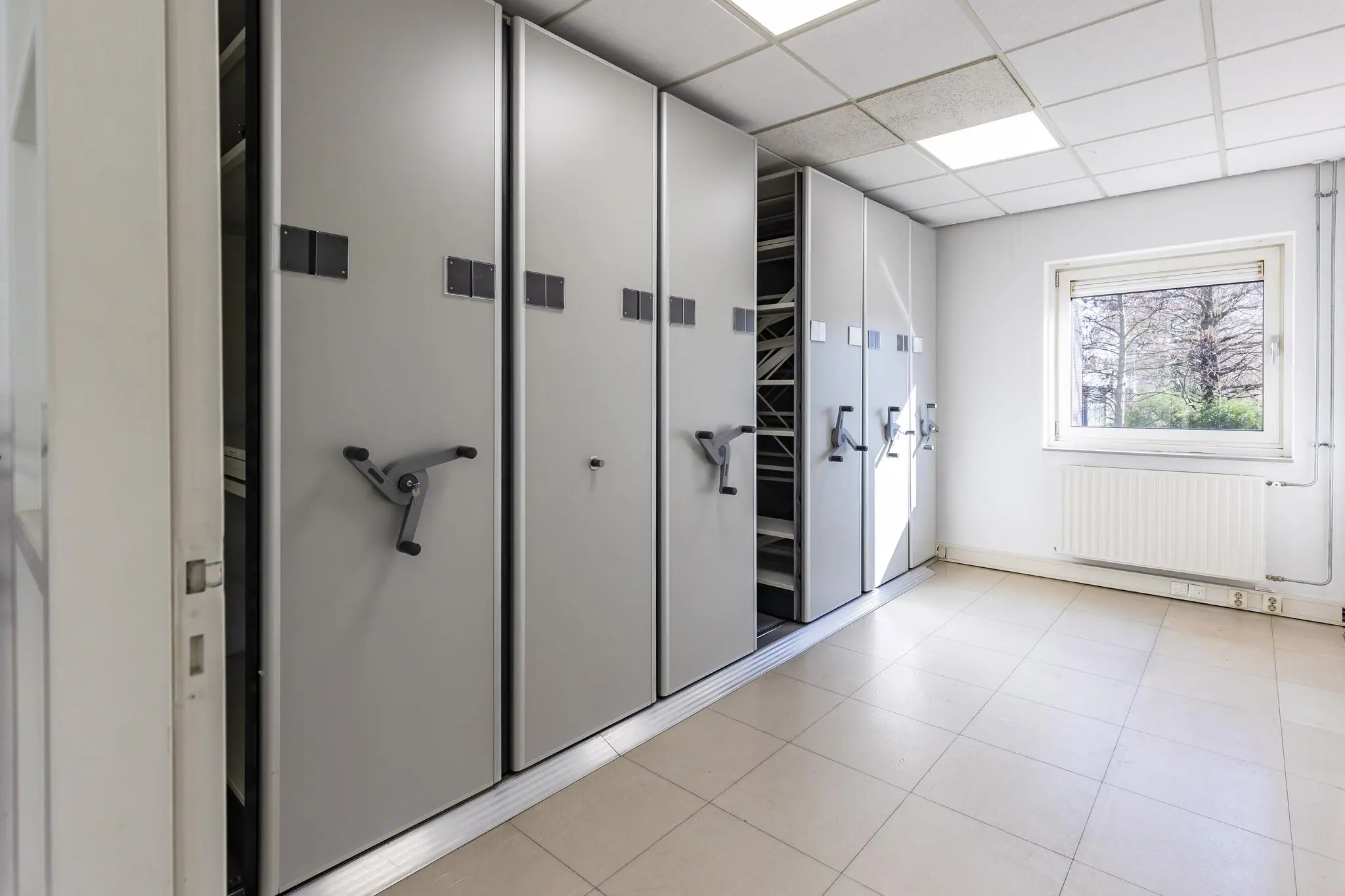 Archiefruimte met verrijdbare ladekasten en een raam met uitzicht op bomen.