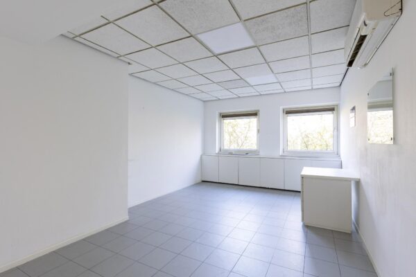 Lege, lichte kantoorruimte aan de ’s-Gravenweg met twee ramen, een systeemplafond en tegelvloer.