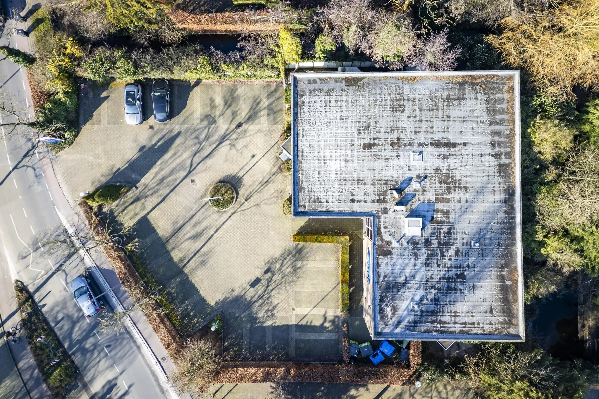 Luchtfoto van een modern gebouw aan de 's-Gravenweg met aangrenzende parkeerplaatsen en omliggende bomen.