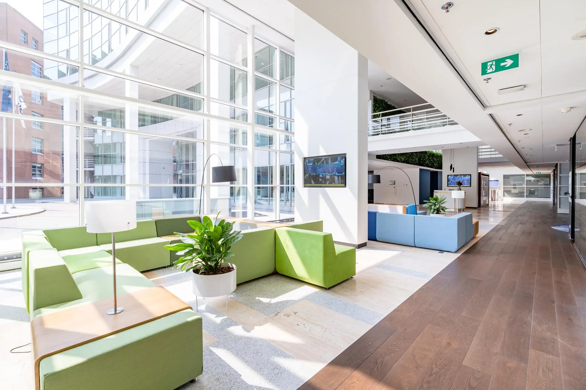 Lichte en moderne kantoorlounge op Newtonlaan met groene en blauwe zithoeken, grote raampartijen en houten vloer.