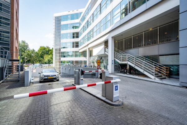Ingang van een ondergrondse parkeergarage bij een modern kantoorgebouw aan de Newtonlaan, met slagboom, fietsenstalling en trappen.
