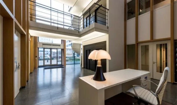 Moderne entreehal van een kantoorgebouw aan de Hogehilweg met ontvangstbalie, designlamp en glazen draaideuren.
