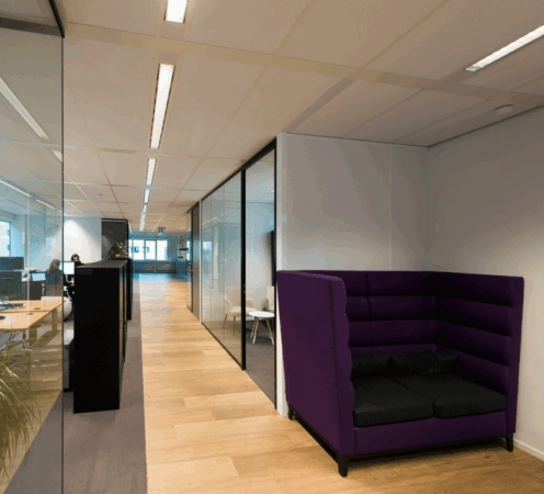 Moderne kantoorruimte aan de Hogehilweg met glazen wanden, houten vloer en een paarse akoestische zithoek.