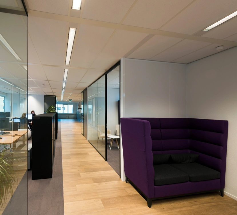 Moderne kantoorruimte aan de Hogehilweg met glazen wanden, houten vloer en een paarse akoestische zithoek.