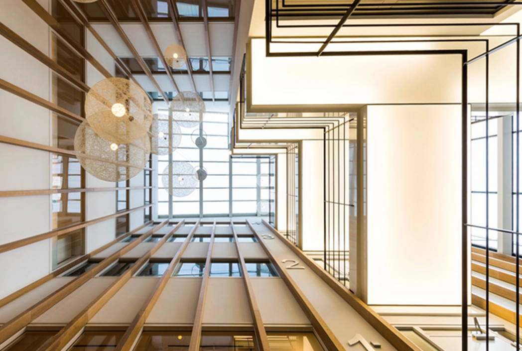 Modern atrium van kantoorgebouw aan de Hogehilweg met houten lamellen, hanglampen en geometrische verlichting.