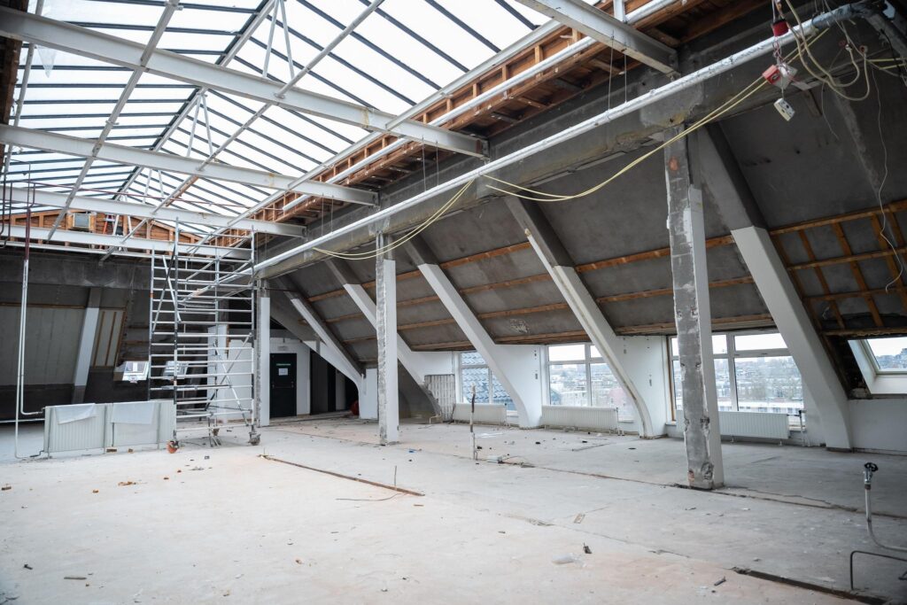 Leegstaande zolderruimte aan het WG-plein in verbouwing met zichtbare dakconstructie en steiger.