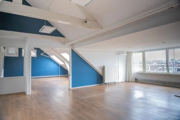 Lichte zolderruimte met houten vloer, blauwe accenten en grote ramen met uitzicht over het WG-Plein.