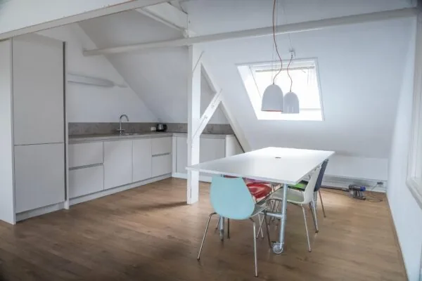 Moderne keuken en eethoek met gekleurde stoelen onder een schuin dak op het WG-plein.