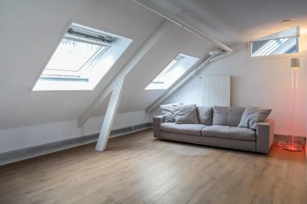 Lichte zolderkamer aan het WG-plein met een grijze bank, houten vloer en dakramen.