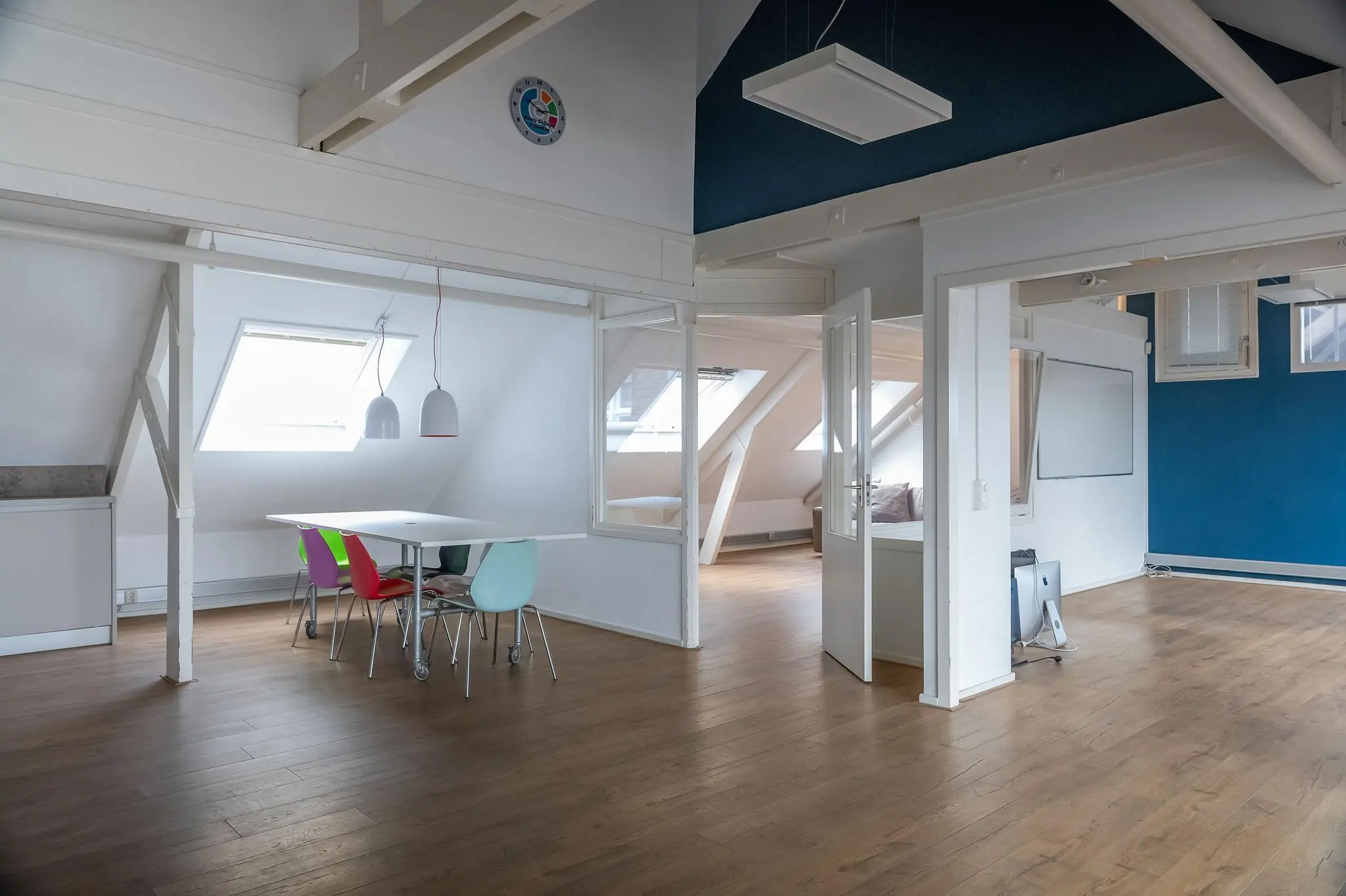 Licht en modern kantoor op het WG-plein met houten vloer, schuine dakramen en kleurrijke stoelen rond een vergadertafel.