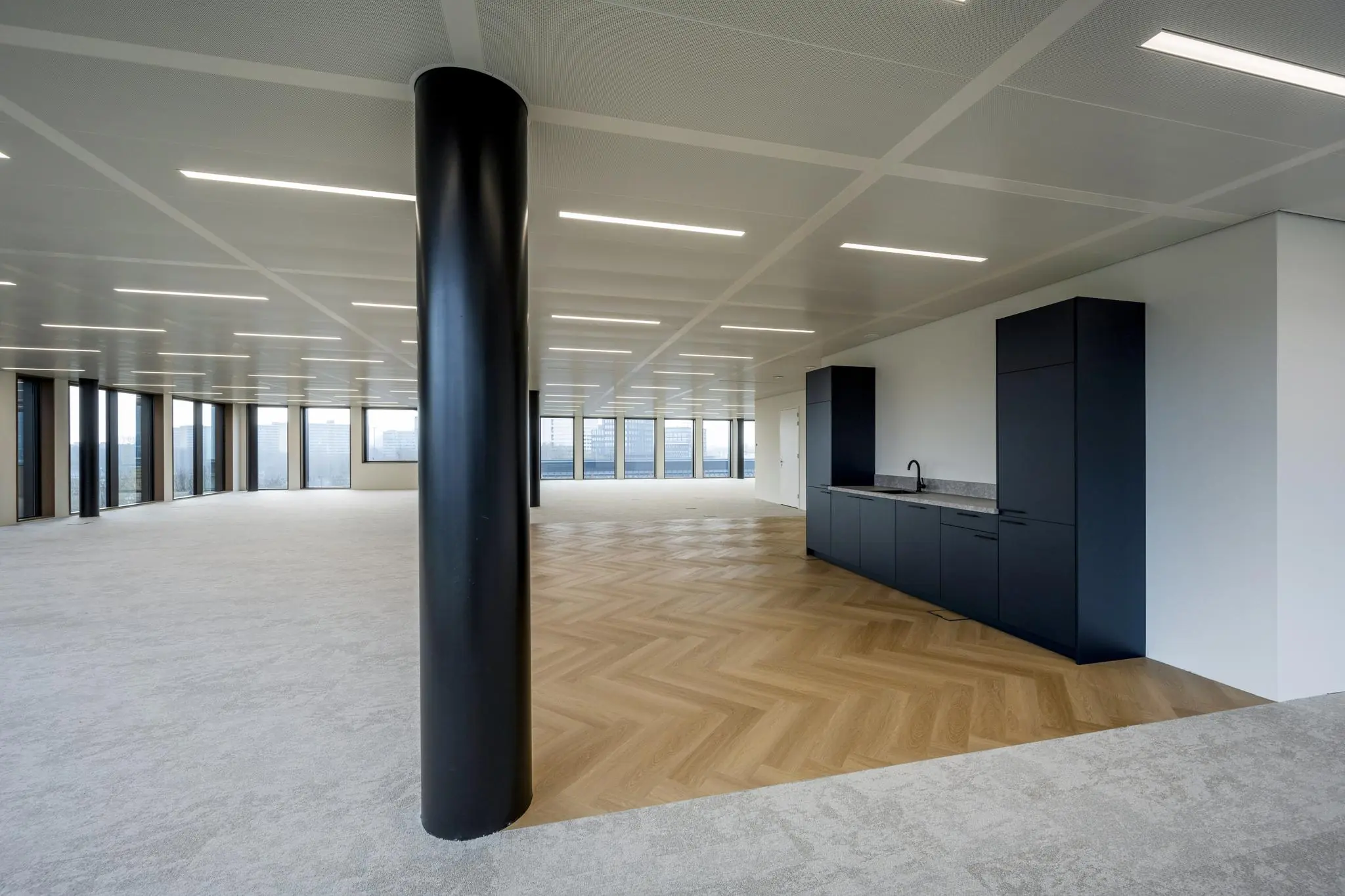 Moderne, open kantoorruimte aan de Gelrestraat met grote ramen, een zwart keukeneiland en een afwisseling van tapijt en visgraat houten vloer.