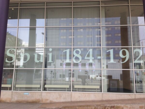 Groot raam met opschrift "Spui 184-192" op een modern kantoorgebouw in een stedelijke omgeving.
