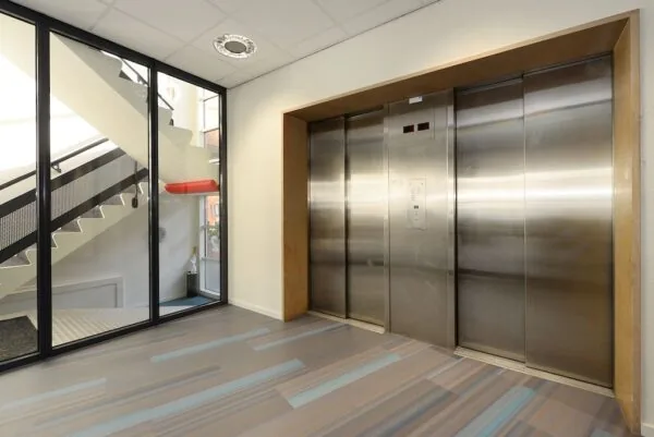 Moderne hal met dubbele roestvrijstalen liften en een glazen wand met zicht op een trap.