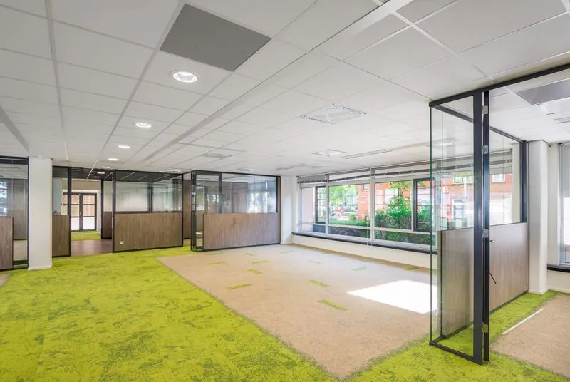Moderne kantoorruimte aan het Spui met glazen scheidingswanden, grote ramen en groen vloerbedekking.
