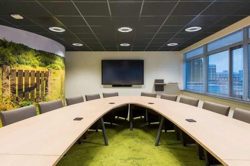 Moderne vergaderruimte aan het Spui met gebogen vergadertafel, groot scherm en wanddecoratie met natuurfoto.