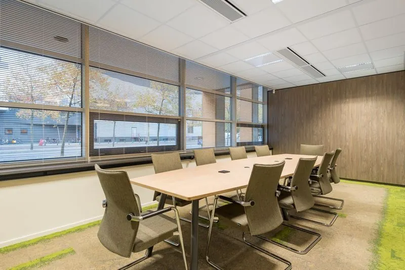 Vergaderruimte met grote tafel, negen stoelen en uitzicht op de straat aan het Spui.