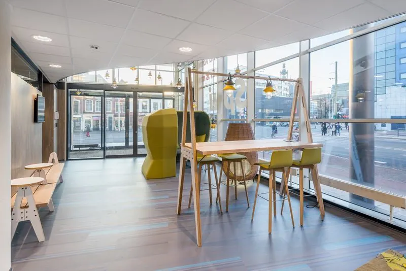 Modern ingerichte wachtruimte aan het Spui met houten meubels, hanglampen en uitzicht op de stad door grote glazen ramen.