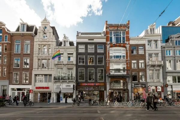 Winkelpandjes aan het Rokin in Amsterdam met kleurrijke gevels, fietserdrukte en een regenboogvlag aan een van de gebouwen.
