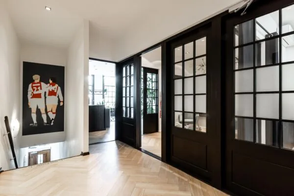 Modern interieur van een kantoor aan het Rokin met zwartmetalen deuren, licht houten visgraatvloer en een muurschildering van twee Ajax-voetballers.