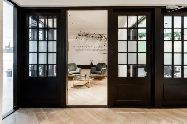 Moderne wachtruimte aan het Rokin met glazen deuren, twee groene fauteuils, een glazen salontafel en een muurquote van Johan Cruijff.