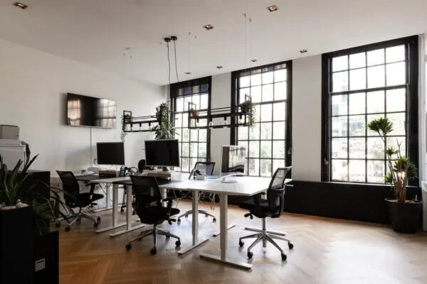 Modern kantoorinterieur aan het Rokin met grote ramen, bureaus met computerschermen en groene planten.