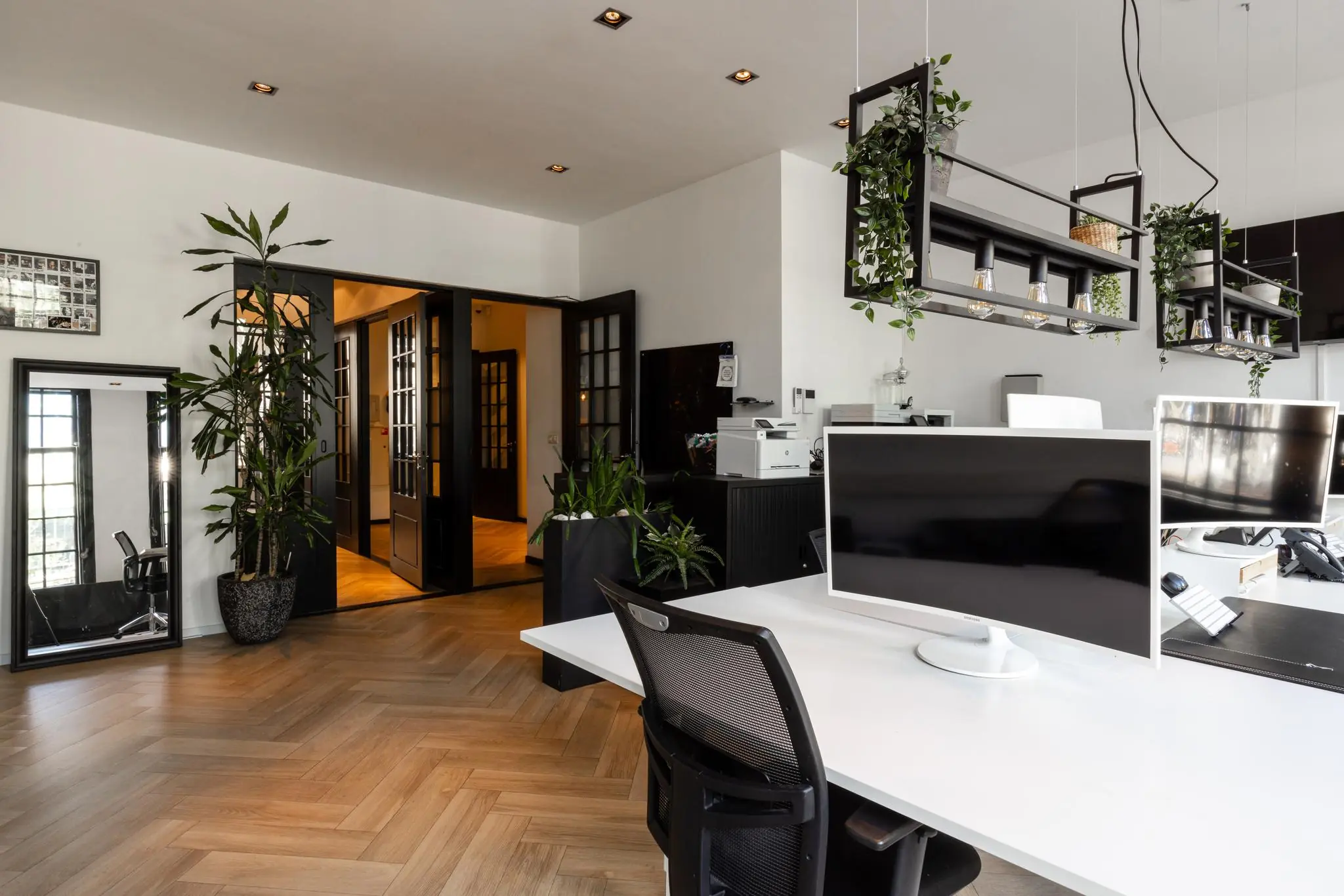 Modern kantoorinterieur aan het Rokin met houten visgraatvloer, zwarte accenten, planten en grote computerschermen.