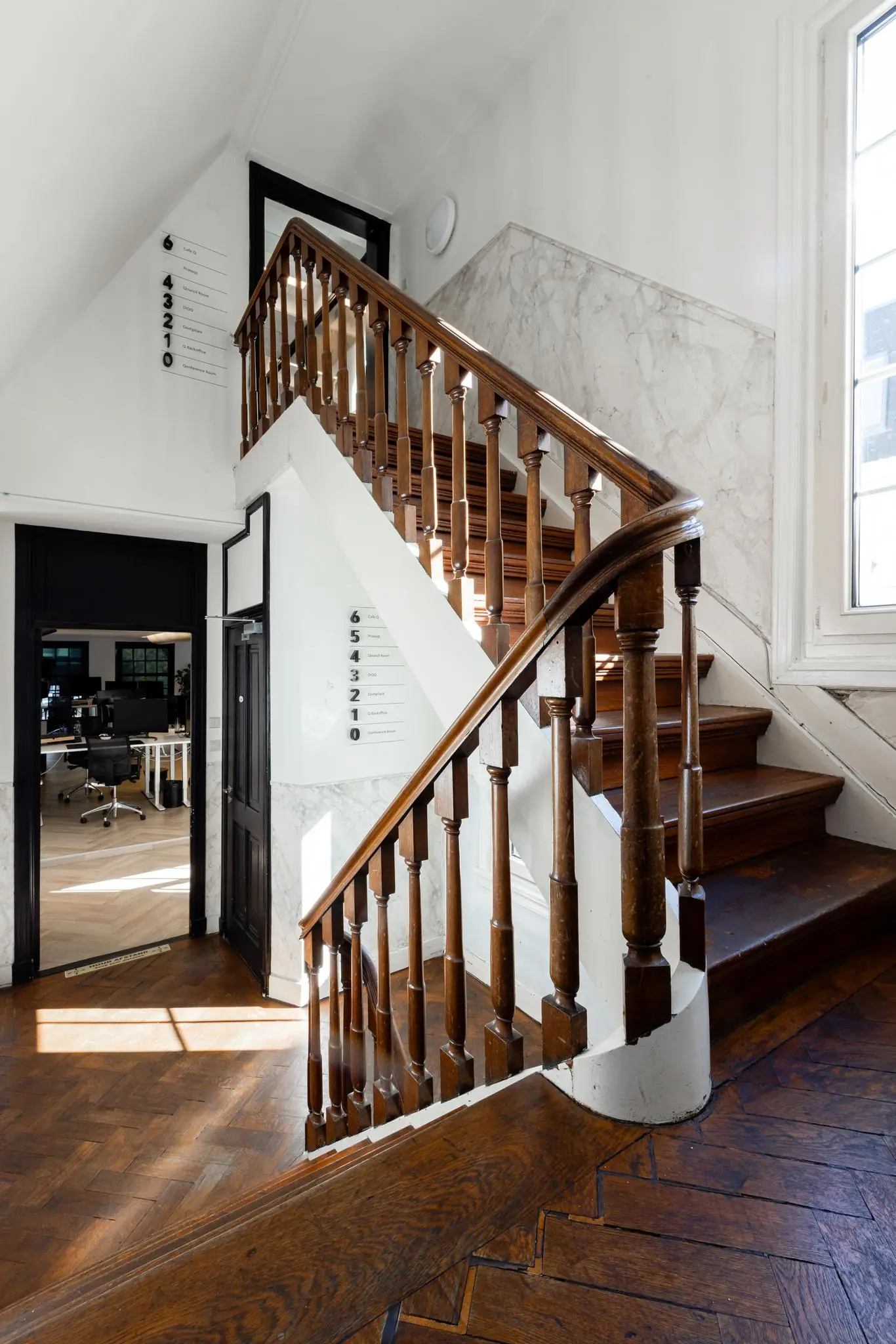 Houten trap met klassiek houten hekwerk in een licht trappenhuis aan het Rokin, met zicht op een modern kantoorinterieur.