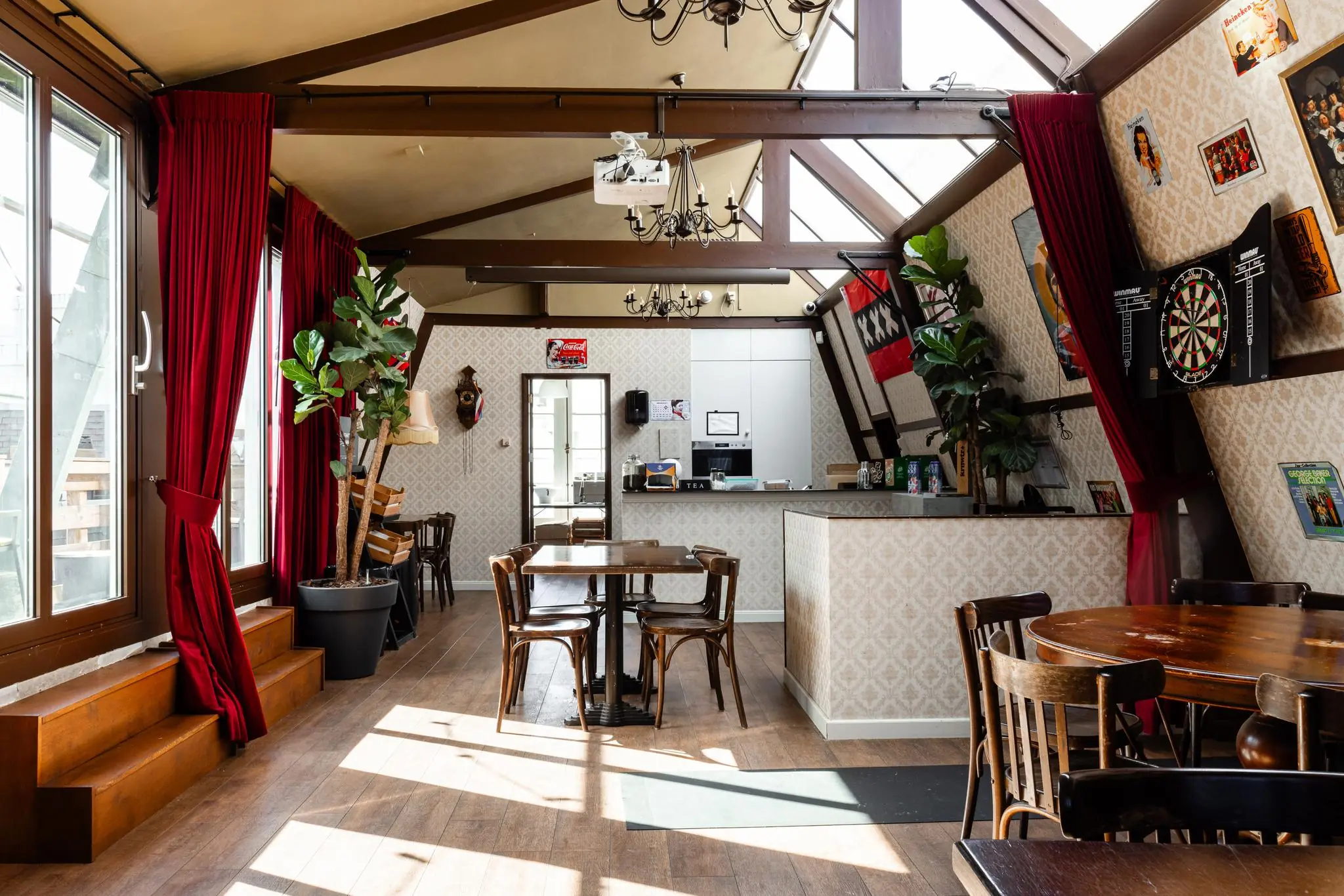 Gezellige horecaruimte aan het Rokin met houten meubels, een bar, dartbord en grote ramen met rode gordijnen.