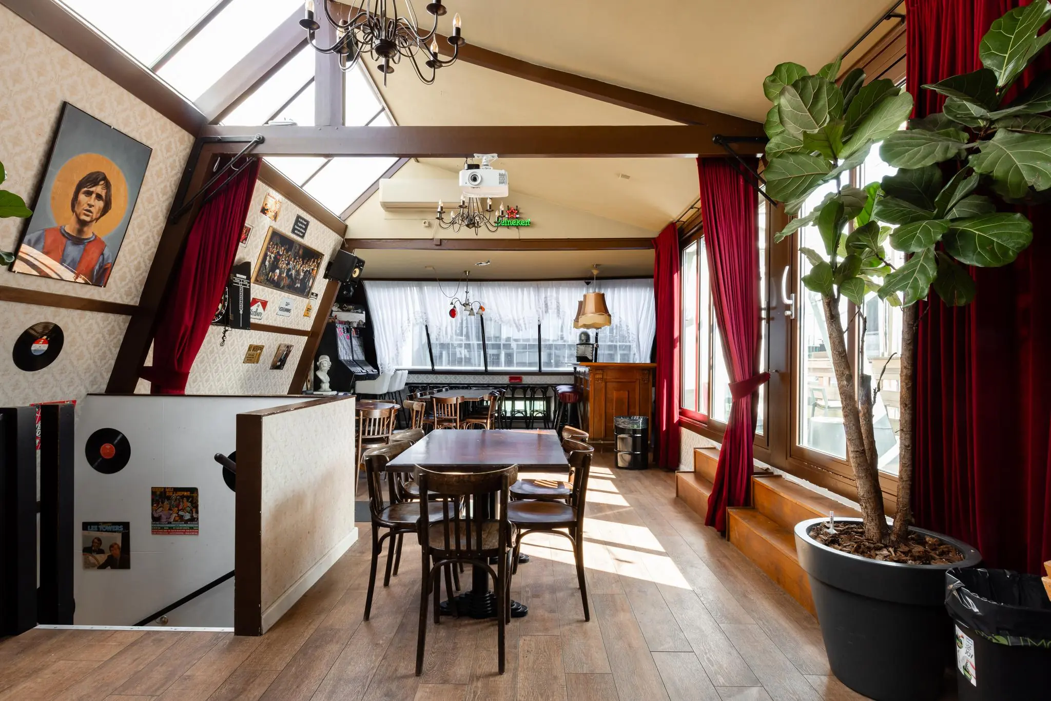 Gezellige, lichtovergoten horecaruimte aan het Rokin met houten vloer, vintage inrichting en grote ramen met rode gordijnen.