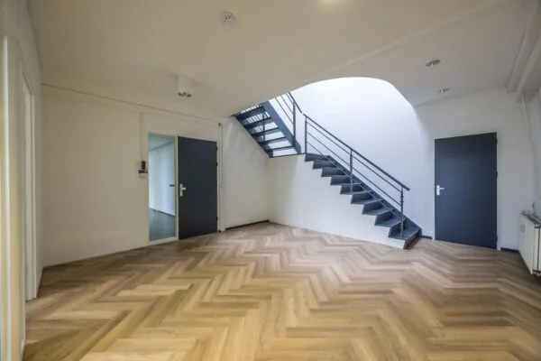 Moderne, lichte hal met visgraat houten vloer, zwarte deuren en een stalen trap naar de bovenverdieping aan de Industrieweg.