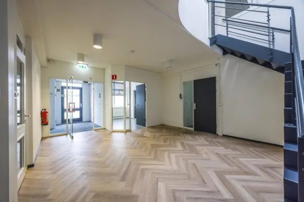 Moderne entreehal van een kantoorpand aan de Industrieweg met visgraatvloer, glazen deuren en zwarte trap.