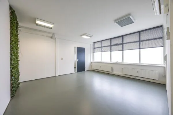 Lichte, lege kantoorruimte aan de Industrieweg met grote ramen, grijze vloer en deels groene wandbekleding.