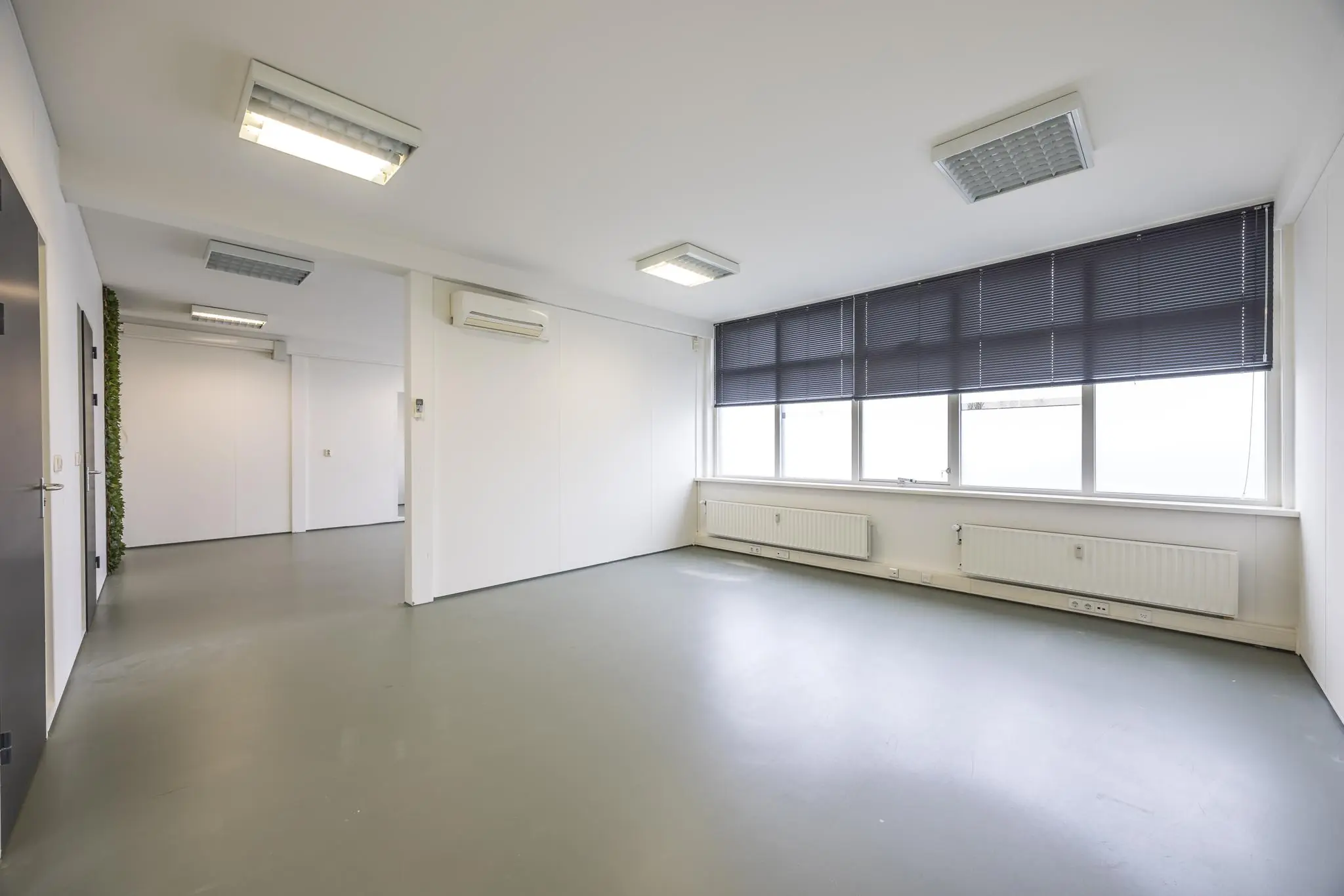 Lichte, lege kantoorruimte aan de Industrieweg met grote ramen, grijze vloer en witte wanden.