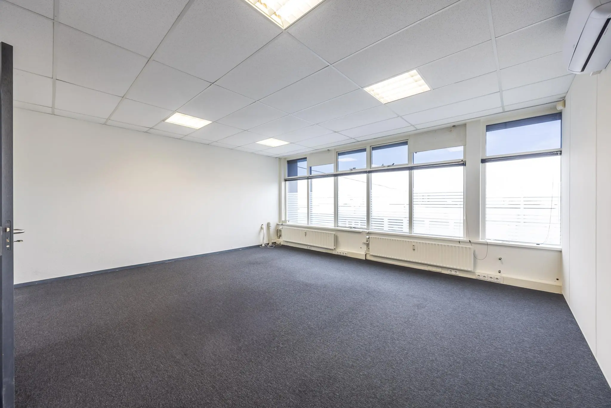 Leeg kantoorruimte met systeemplafond, grijze vloerbedekking en grote ramen aan de Industrieweg.