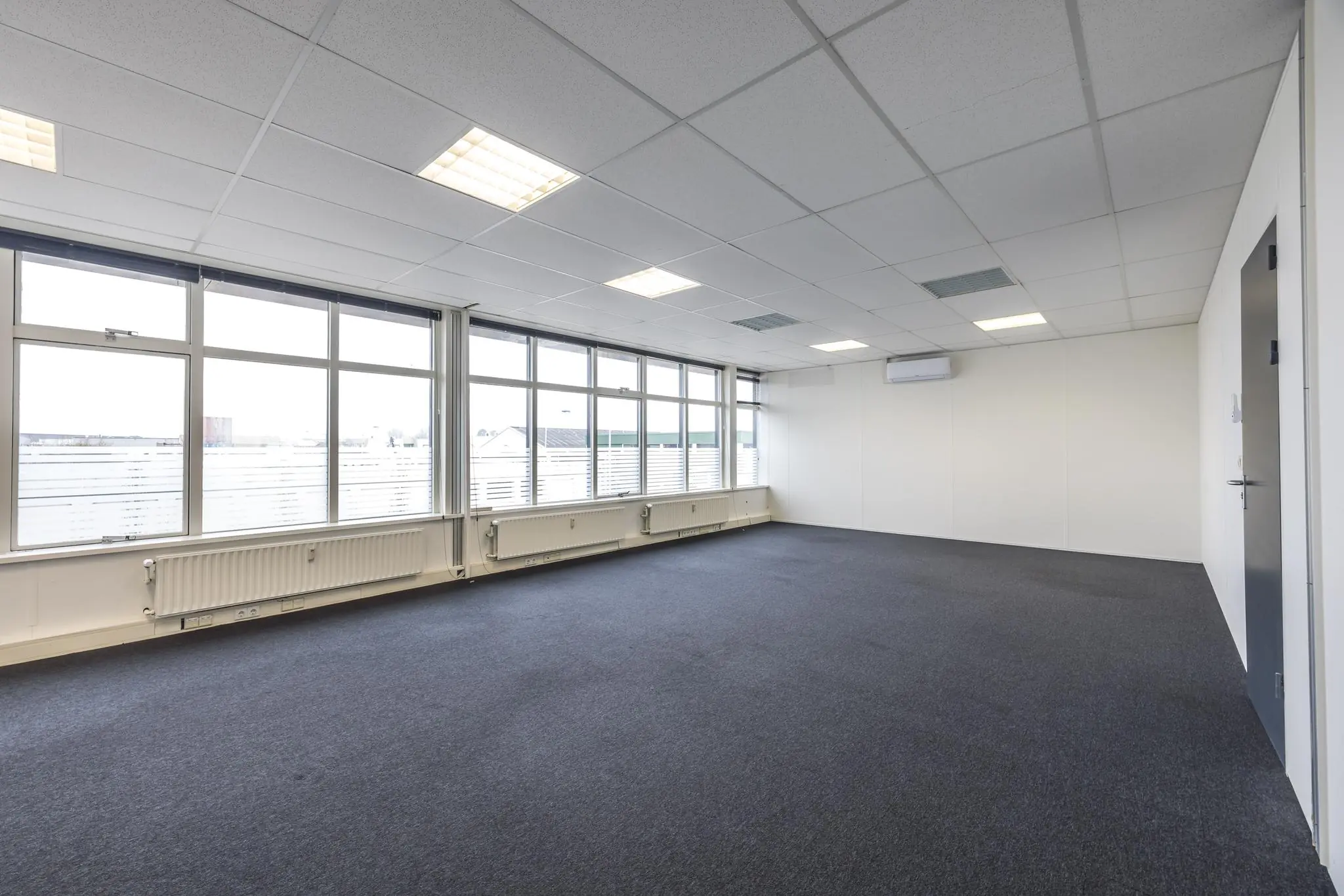 Licht en leeg kantoorpand aan de Industrieweg met grote ramen en systeemplafond.