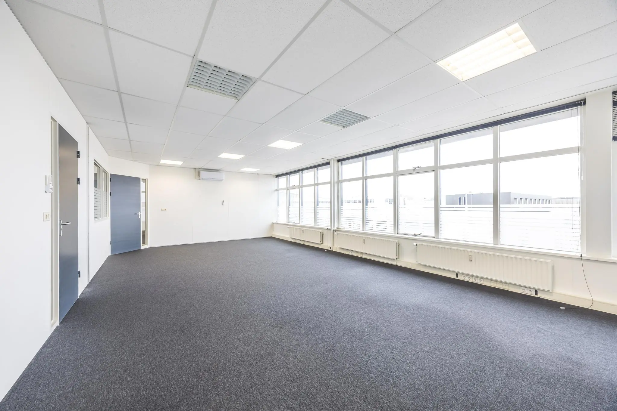 Lichte, lege kantoorruimte aan de Industrieweg met grote ramen en grijze vloerbedekking.