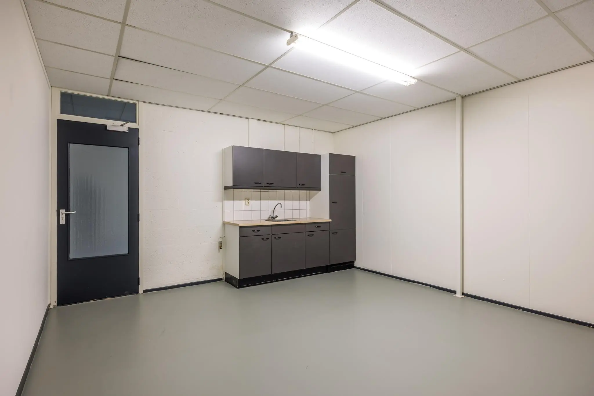 Kleine, eenvoudige kitchenette in een lege, witte bedrijfsruimte aan de Industrieweg.