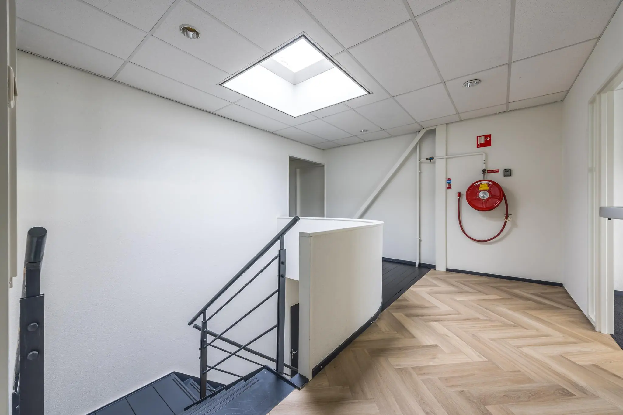 Binnenruimte van een modern bedrijfsgebouw met een trap, lichtkoepel en brandslanghaspel aan de muur.