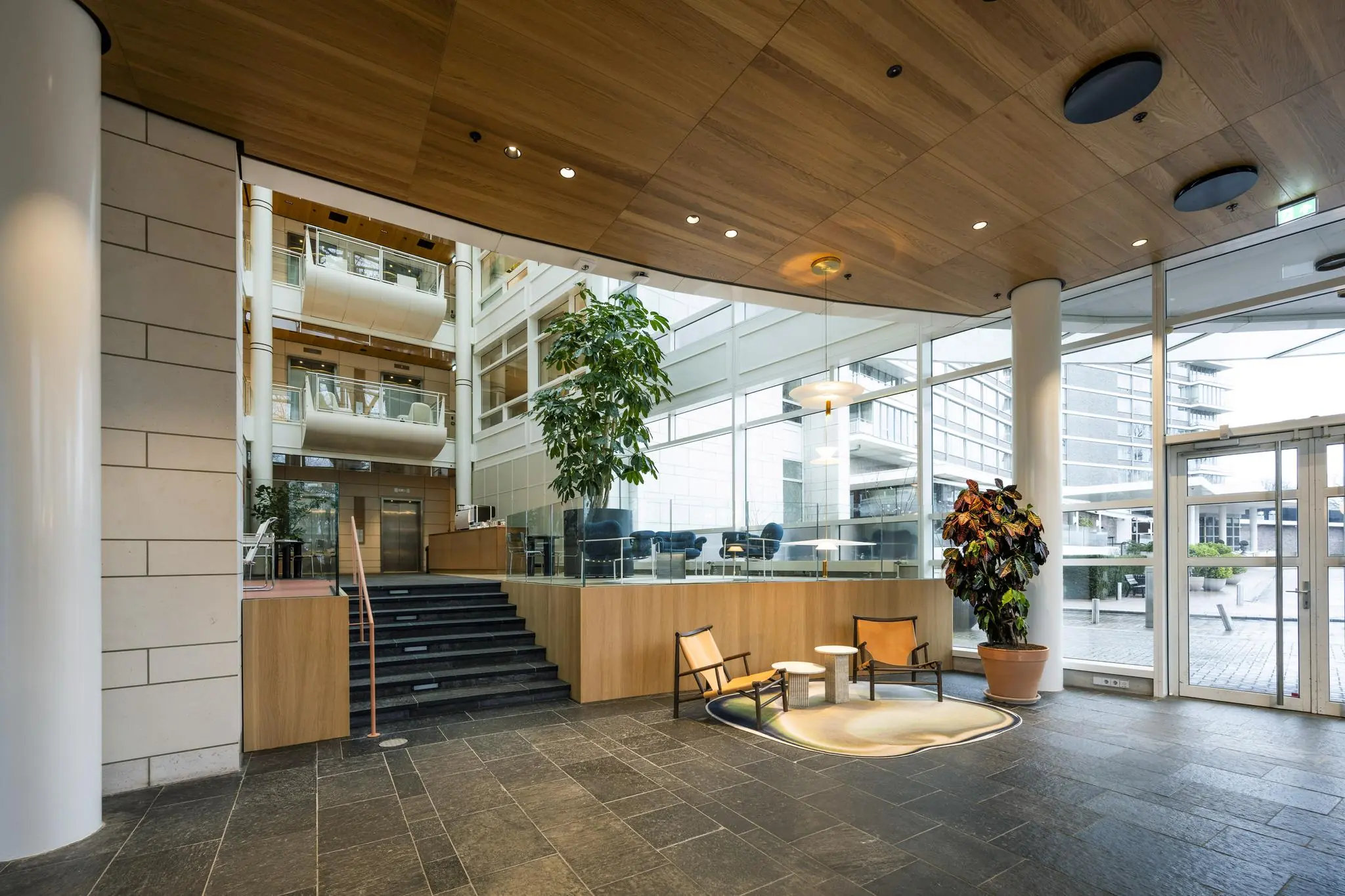Moderne en lichte entreehal van een kantoorgebouw aan de Apollolaan, met zitgelegenheid, planten en een glazen gevel.