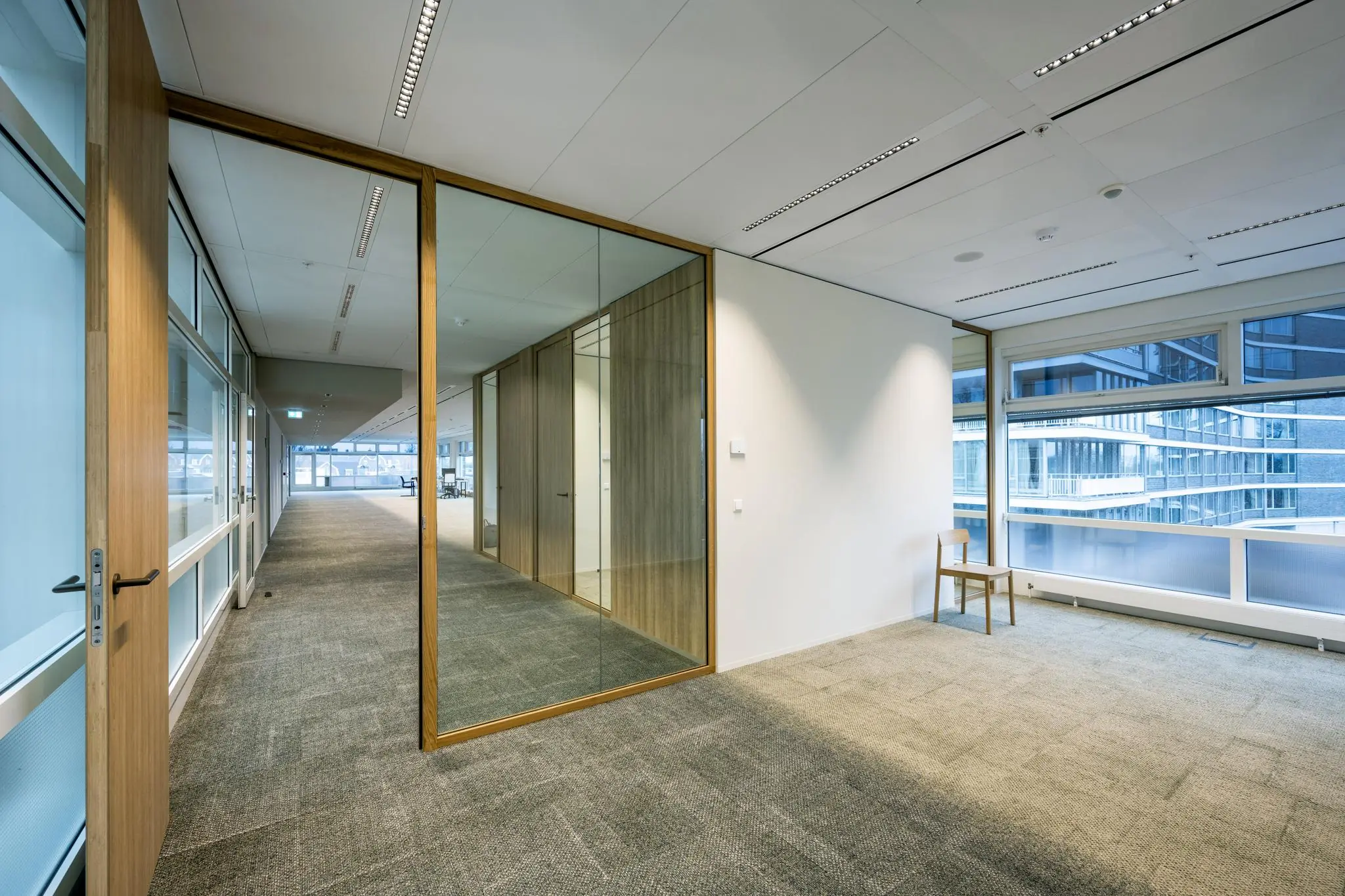 Lichte en moderne kantoorruimte aan de Apollolaan met glazen wanden, houten details en uitzicht op nabijgelegen gebouwen.