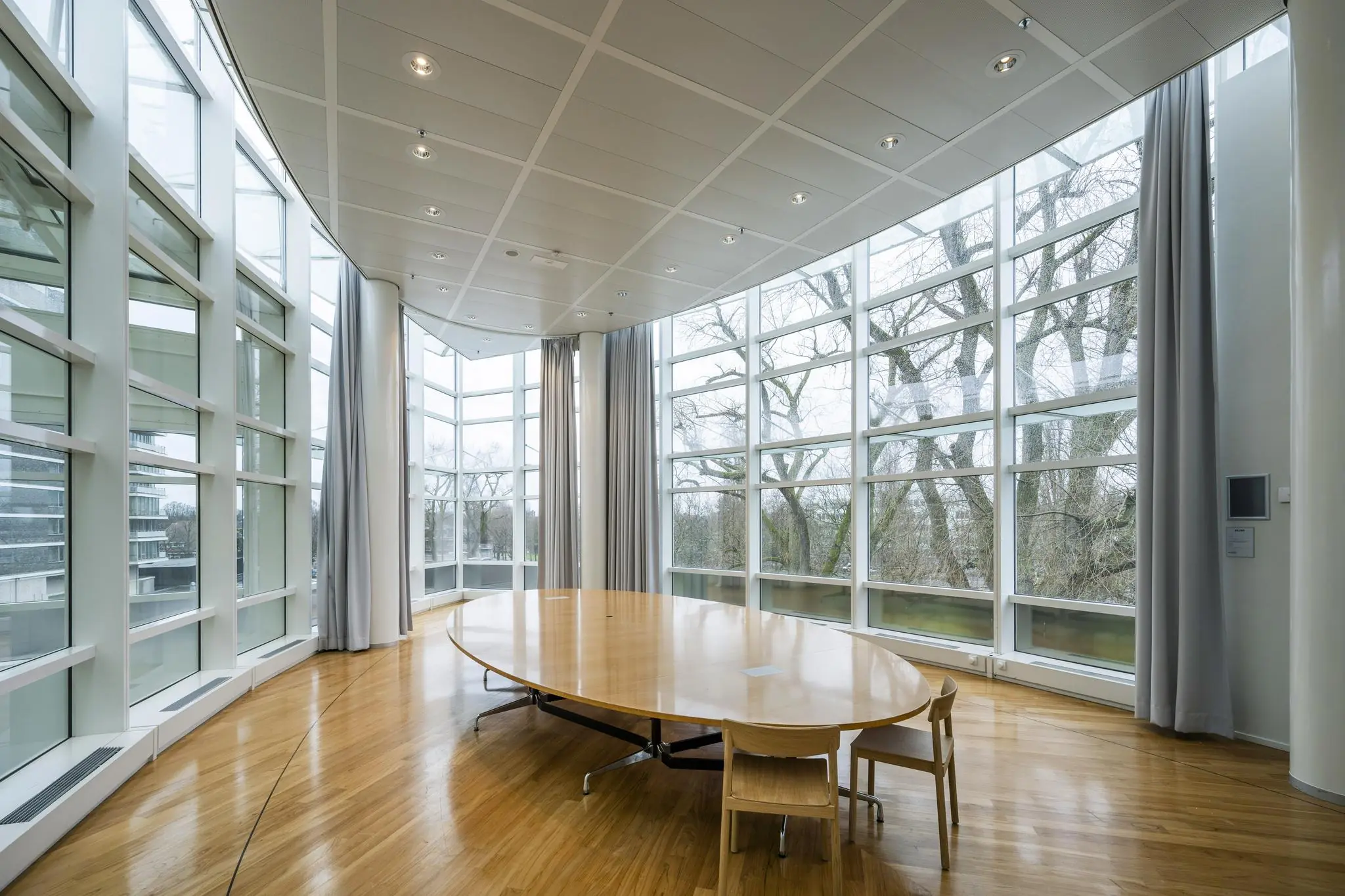 Vergaderruimte met ovale houten tafel en grote ramen aan de Apollolaan.