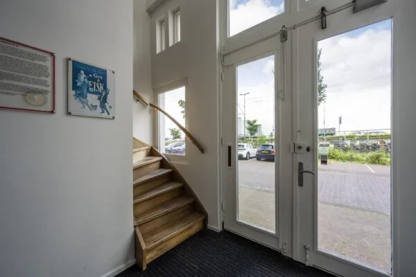 Ingang met houten trap, glazen deur en uitzicht op parkeerplaats aan de De Ruijterkade.