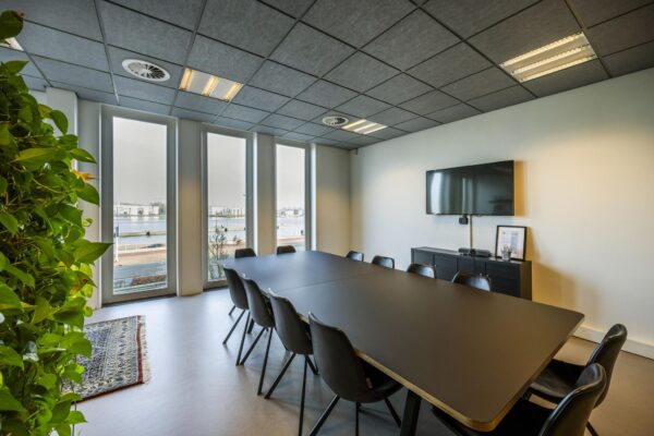 Moderne vergaderruimte aan de De Ruijterkade met uitzicht op het water, een lange tafel, televisie en grote raampartijen.