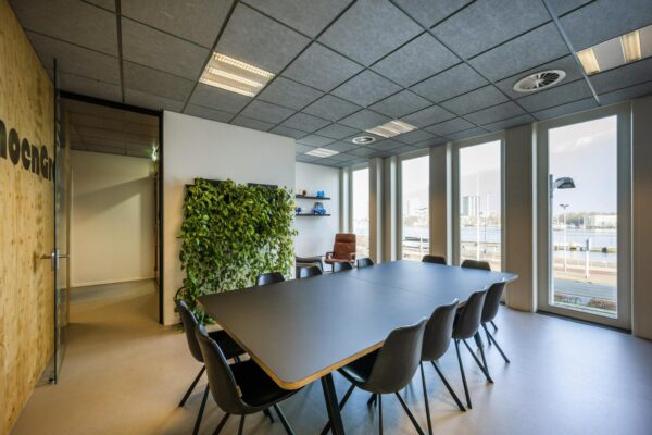 Vergaderruimte aan de De Ruijterkade met een grote tafel, moderne stoelen, groene plantenwand en uitzicht op het water.