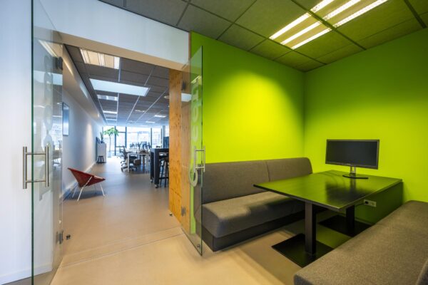 Moderne kantoorruimte aan de De Ruijterkade met een felgroene vergaderruimte voorzien van zitbanken en een monitor.