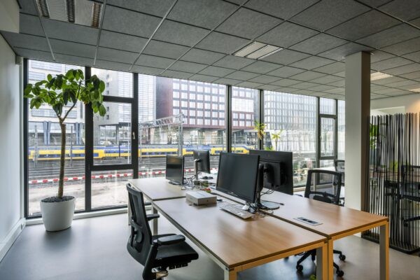Modern kantoorinterieur met uitzicht op spoorlijn en gebouwen aan de De Ruijterkade in Amsterdam.