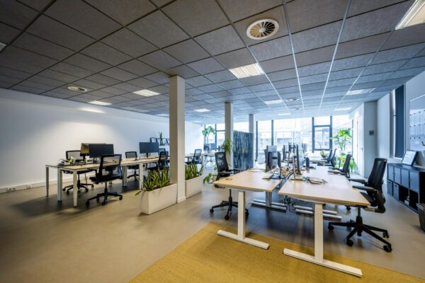 Moderne, open kantoorruimte aan de De Ruijterkade met bureaus, computerschermen en veel natuurlijk licht.