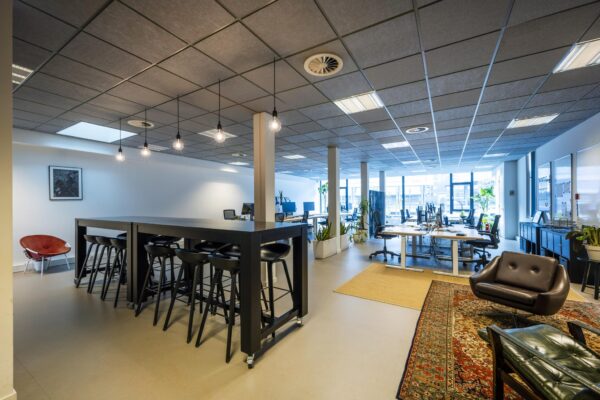 Moderne en open kantoorruimte aan de De Ruijterkade met werkplekken, hoge tafel met barkrukken en een loungehoek.