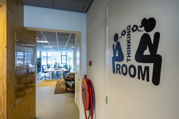 Ingang van een modern kantoor aan de De Ruijterkade met op de voorgrond een deur met het opschrift "Thinking Room" en grappige pictogrammen.