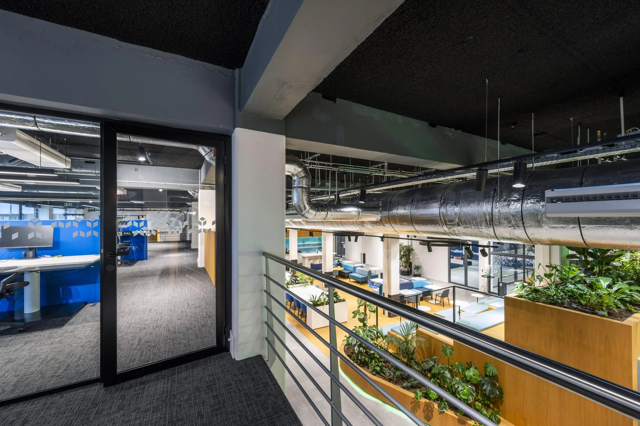 Modern kantoorinterieur aan de Kabelweg met open werkplekken, veel groen en industriële plafondbuizen.